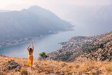 Rear view girl raises her hands up. She admires the city of Kotor in Montenegro and shows how happy she is.