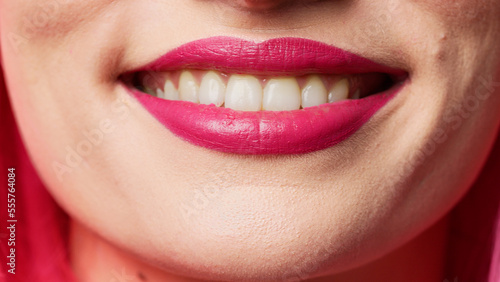 Cheerful female model showing candid smile in studio, wearing glamour pink lipstick and smiling. Beautiful attractive person acting flirty expressing passion. Macro shot, extreme closeup.