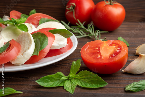 Italian caprese salad tomato basil mozzarella, in a plate on a wooden table