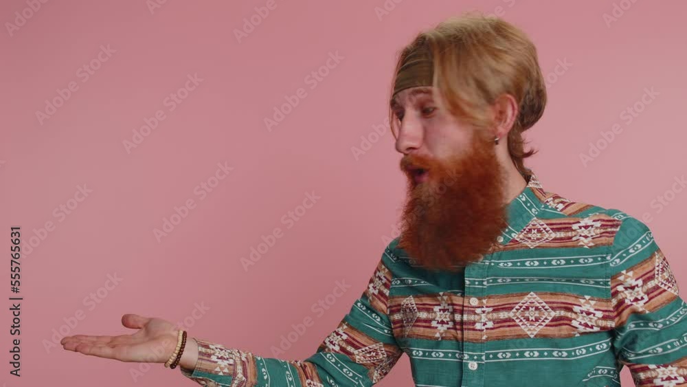 Hippie redhead bearded man in pattern shirt showing thumbs up and pointing at left on blank space. Place for your commercial advertisement logo, banner, text. Hipster ginger guy boy on pink background Hippie redhead bearded man in pattern shirt showing thumbs up and pointing at left on blank space. Place for your commercial advertisement logo, banner, text. Hipster ginger guy boy on pink background