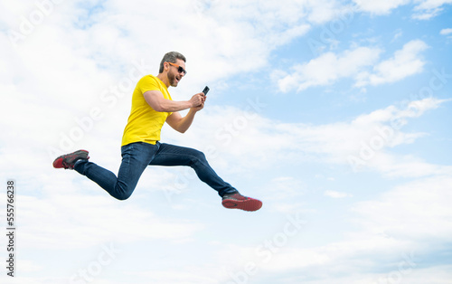 man jumping and chatting on smartphone on sky background. copy space