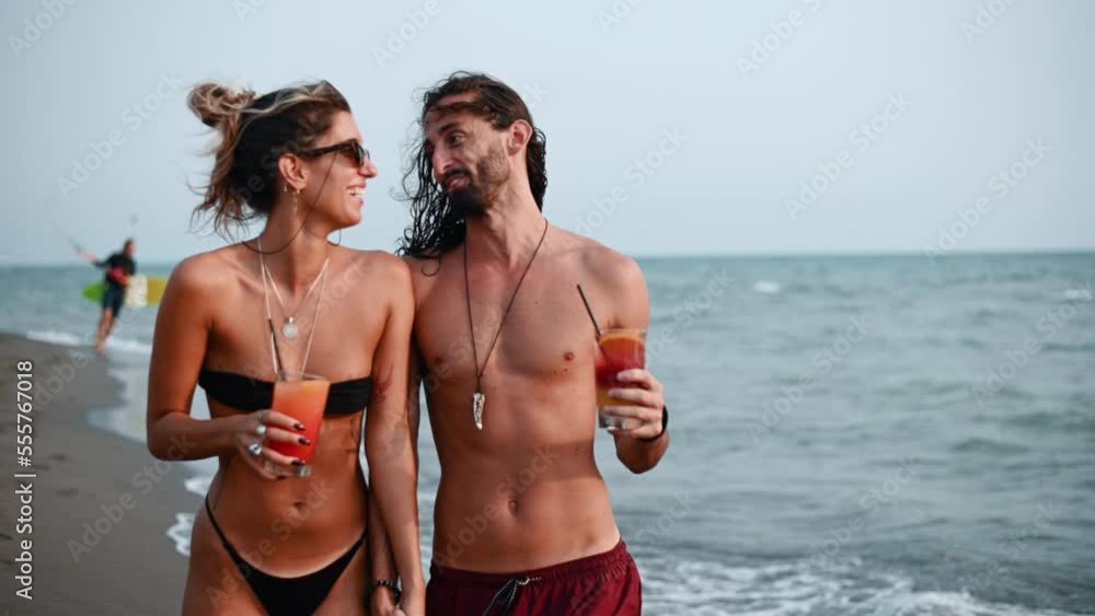 Young couple with alcohol cocktails walking on the beach Young couple with alcohol cocktails walking on the beach