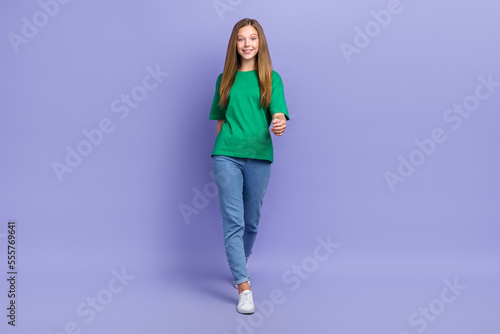 Full length photo of charming adorable small lady wear green t-shirt smiling walking isolated violet color background