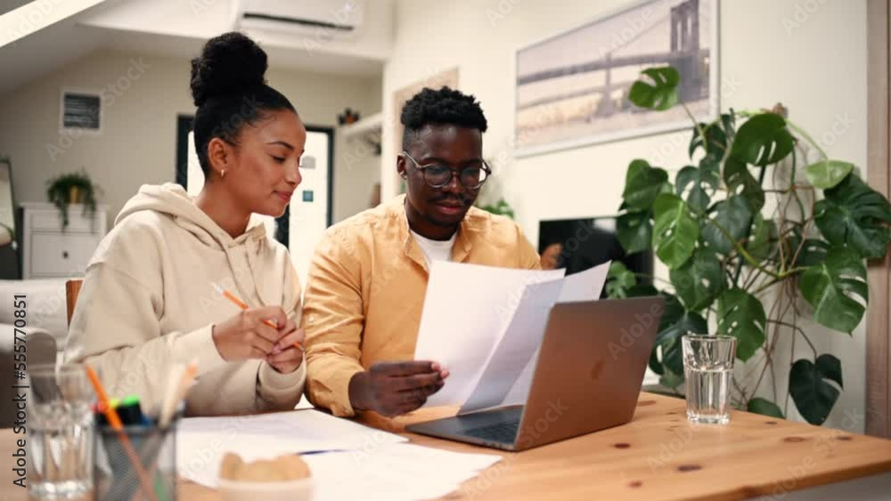 Diverse couple using a laptop and papers and documents at home Diverse couple using a laptop and papers and documents at home