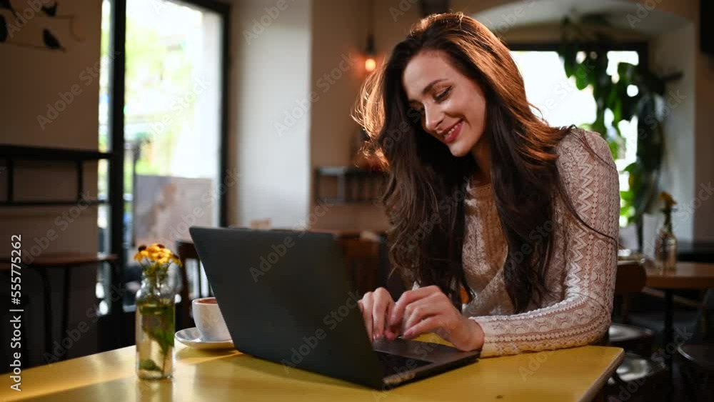 Woman with natural makeup using laptop while working remotely in a cafe Woman with natural makeup using laptop while working remotely in a cafe