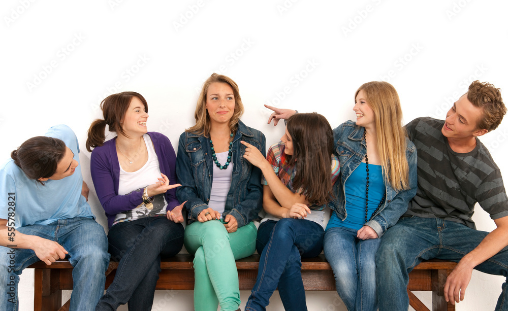 Six, young men and women sitting on bench together, laughing and looking at each other, studio shot on white background Six, young men and women sitting on bench together, laughing and looking at each other, studio shot on white background