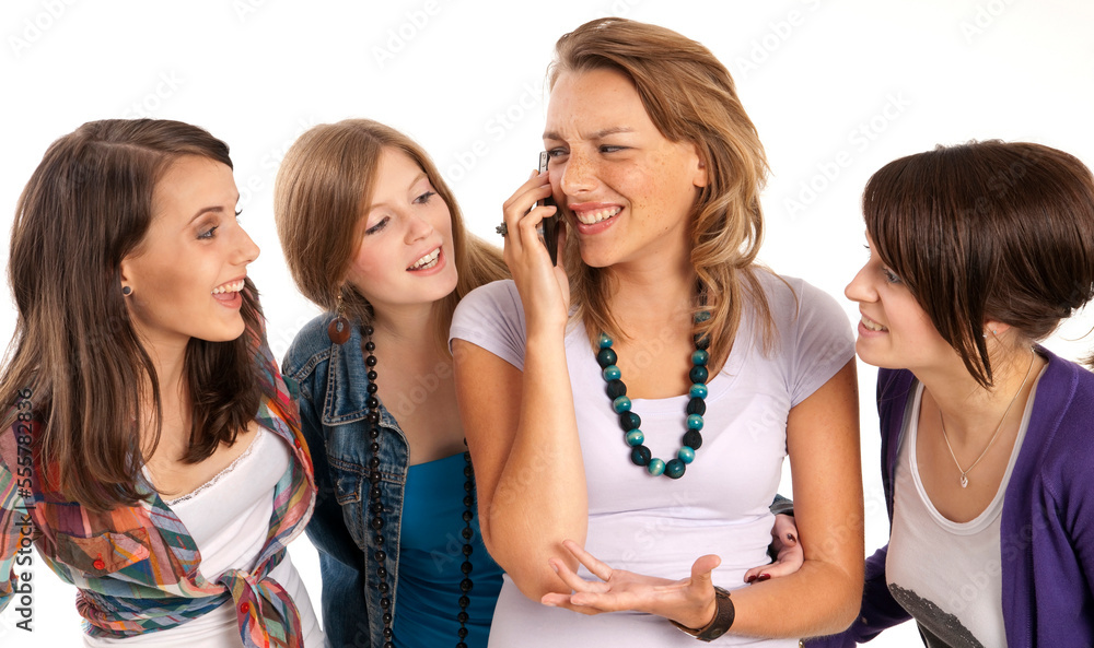 Four, young women laughing and looking at each other, one young woman using cell phone, studio shot on white background Four, young women laughing and looking at each other, one young woman using cell phone, studio shot on white background