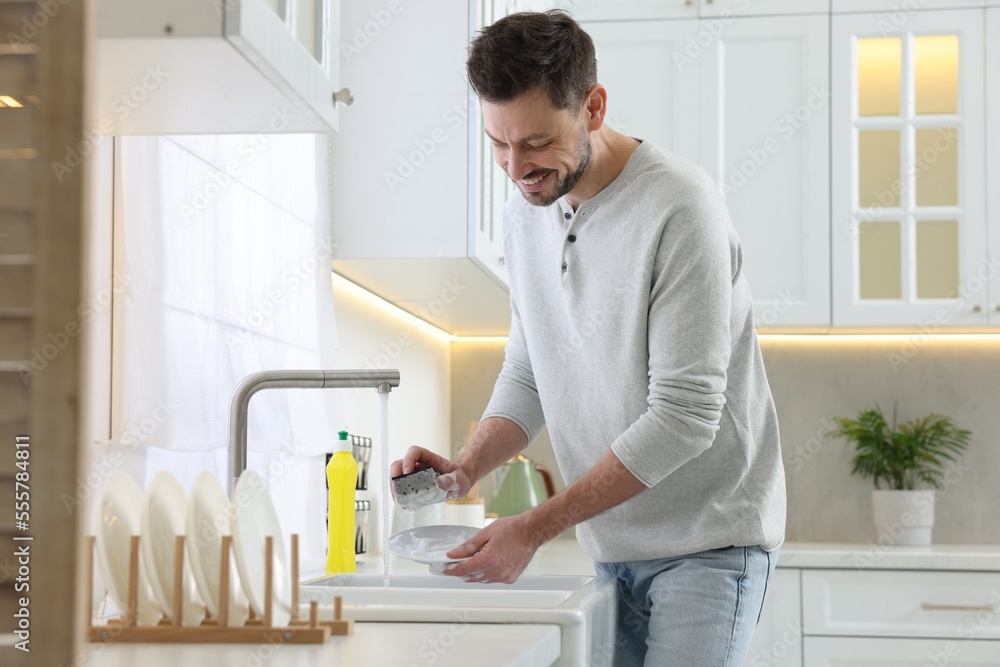 Man washing plate above sink in kitchen Man washing plate above sink in kitchen