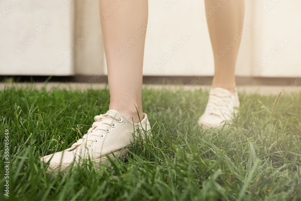 Woman in stylish sneakers walking on green grass outdoors, closeup