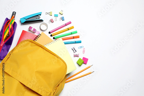 Backpack with different school stationery on white background, flat lay. Space for text