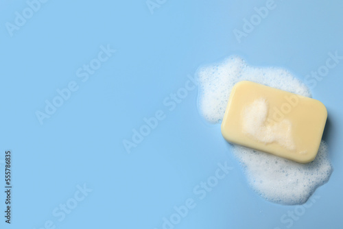 Soap and fluffy foam on light blue background, top view. Space for text