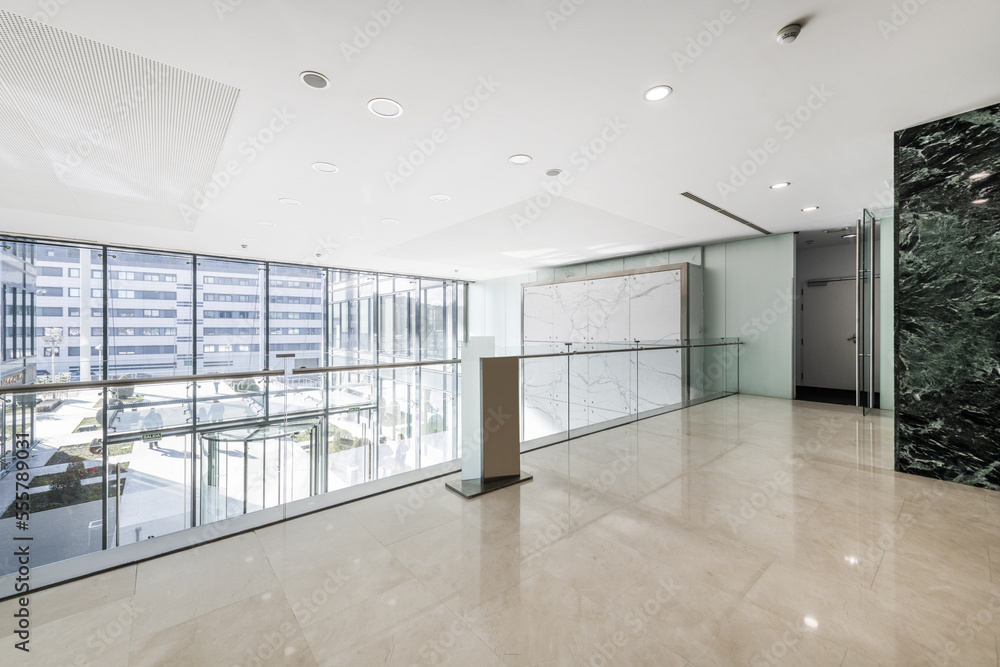 Atrium of an office building with green marble tiled walls, cream marble floors viewed from a large mezzanine window with a glass railing and a revolving door at the entrance Atrium of an office building with green marble tiled walls, cream marble floors viewed from a large mezzanine window with a glass railing and a revolving door at the entrance