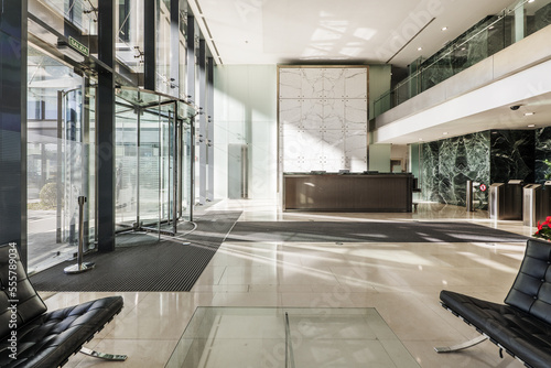 Atrium of an office building with green marble tiled walls  cream marble floors and a reception desk next to a revolving door at the entrance