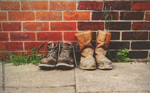 Two pairs of old boots in front of a  brick wall.The boots are heavily worn steel toe cap safety boots.