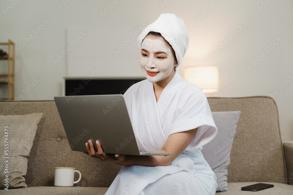 Young pretty asian woman with facial mask sitting on sofa puts nourishing mask on skin for rejuvenating and eliminating defects. Acne. Smile. Young pretty asian woman with facial mask sitting on sofa puts nourishing mask on skin for rejuvenating and eliminating defects. Acne. Smile.