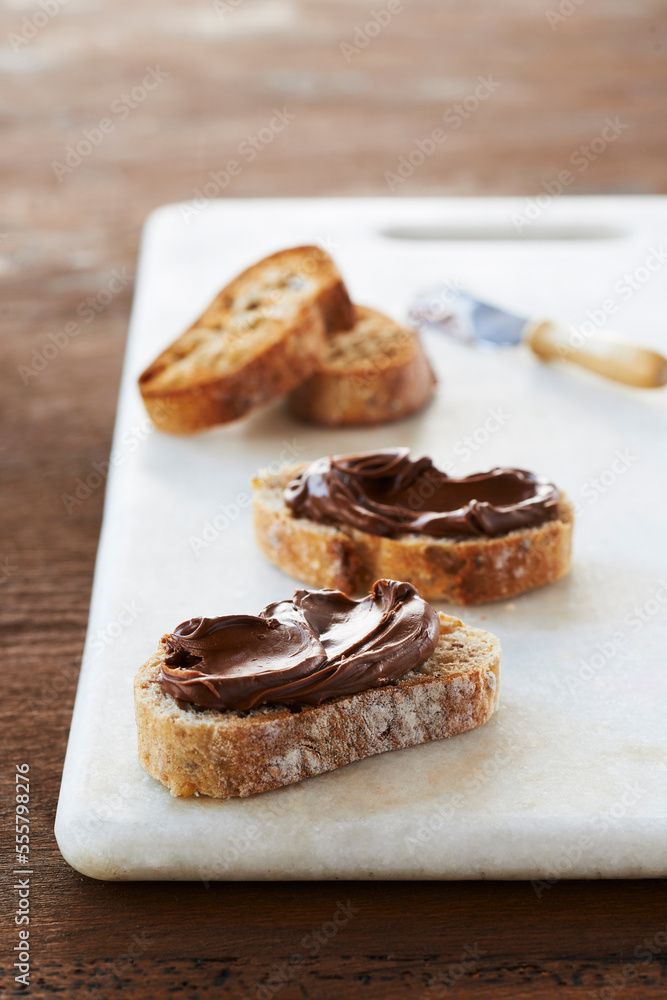 Slices of Baguette topped with Hazelnut Spread on Marble Slab on Wooden Background, Studio Shot Slices of Baguette topped with Hazelnut Spread on Marble Slab on Wooden Background, Studio Shot