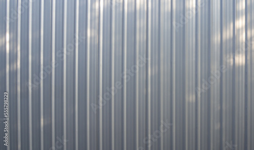 Vertical silver metal sheet pattern and tree shadows.