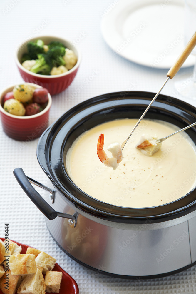 Cheese fondue in slowcooker with shrimp, bread and vegetables Cheese fondue in slowcooker with shrimp, bread and vegetables
