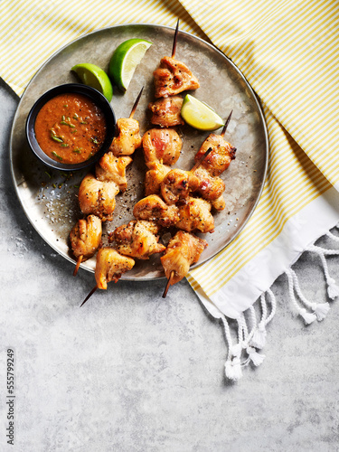 Chicken satay skewers with dipping sauce and lime wedges on a metal tray on striped fabric photo