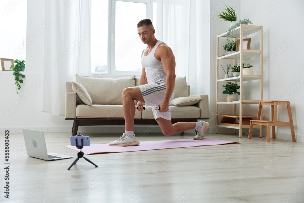 Man sports, watching a workout tape on his phone and repeating exercises sports blogger with dumbbells, pumped up man fitness trainer works out at home, the concept of health and body beauty Man sports, watching a workout tape on his phone and repeating exercises sports blogger with dumbbells, pumped up man fitness trainer works out at home, the concept of health and body beauty