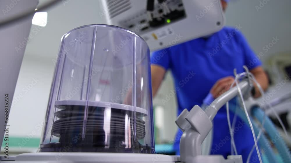 Pump of artificial ventilator machine raising inside the capsule. Doctor at backdrop is watching the work of equipment. Low angle view. Pump of artificial ventilator machine raising inside the capsule. Doctor at backdrop is watching the work of equipment. Low angle view.