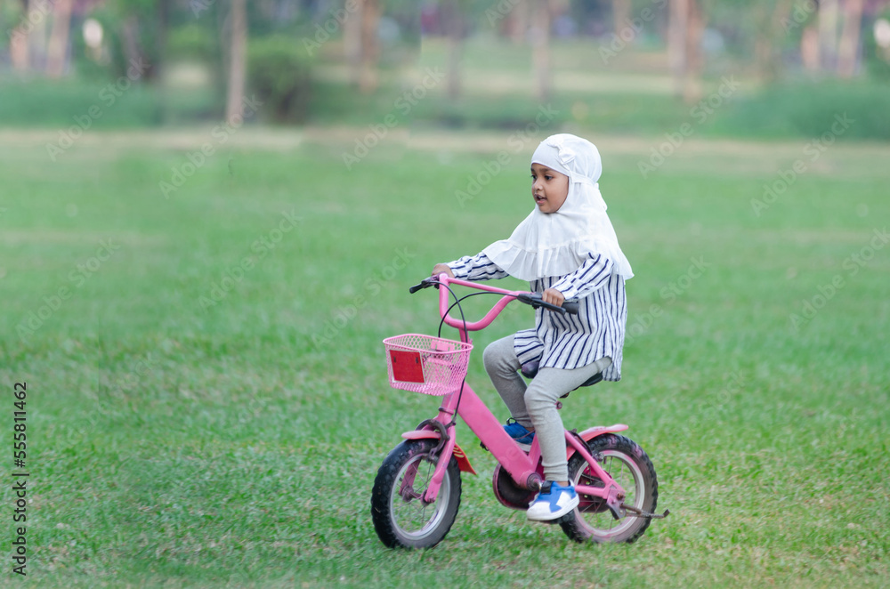 Happy Muslim little girl riding bicycle in green lawn park Happy Muslim little girl riding bicycle in green lawn park