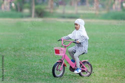 Happy Muslim little girl riding bicycle in green lawn park