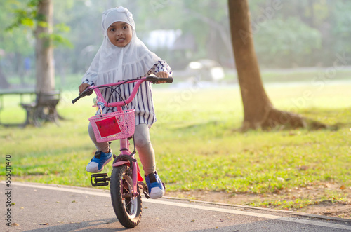 Fototapeta Naklejka Na Ścianę i Meble -  Smiling Muslim little girl riding bicycle in the park, in autumn park at sunset
