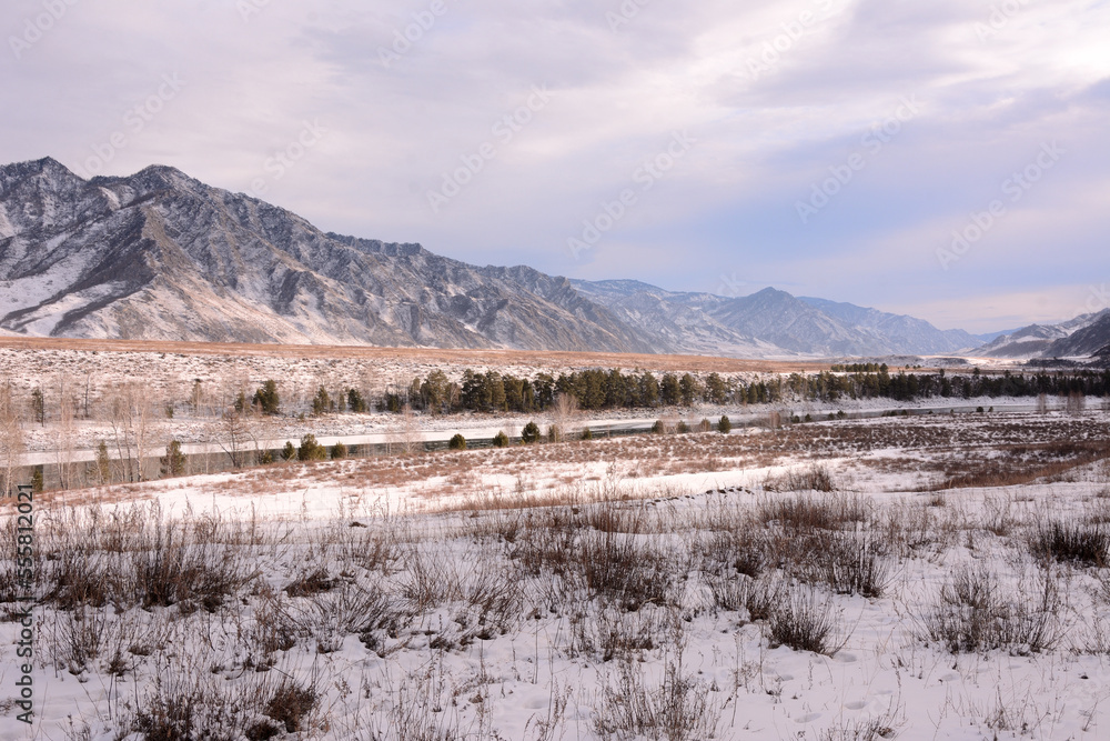 Snow-covered valley with low dry grass surrounded by high mountains in early winter. Snow-covered valley with low dry grass surrounded by high mountains in early winter.