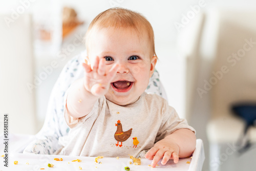 Happy baby smiling in high chair pointing with scraps of food photo
