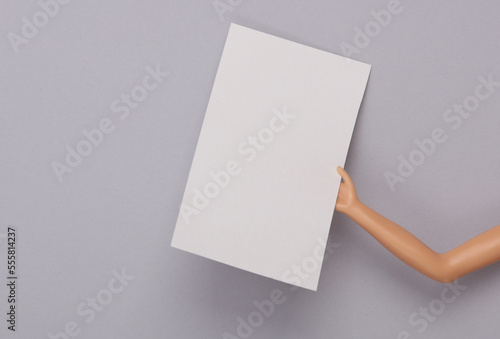 Doll's hand holding a white empty business card on a gray background