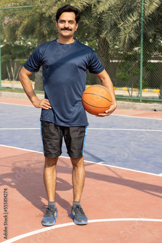 Portrait of a young man holding a basketball ball at the outdoor courtyard.