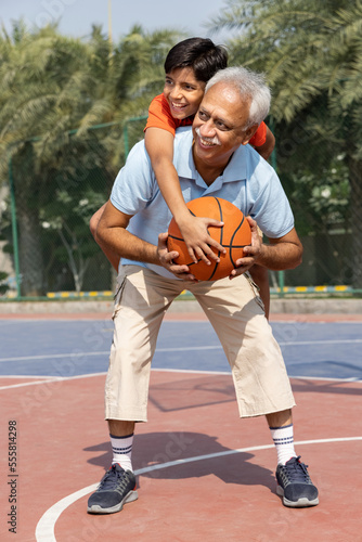 Grandfather and his grandson enjoying and playing together on basketball court.
