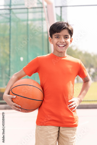 A portrait of a boy kid playing with a basketball in court.