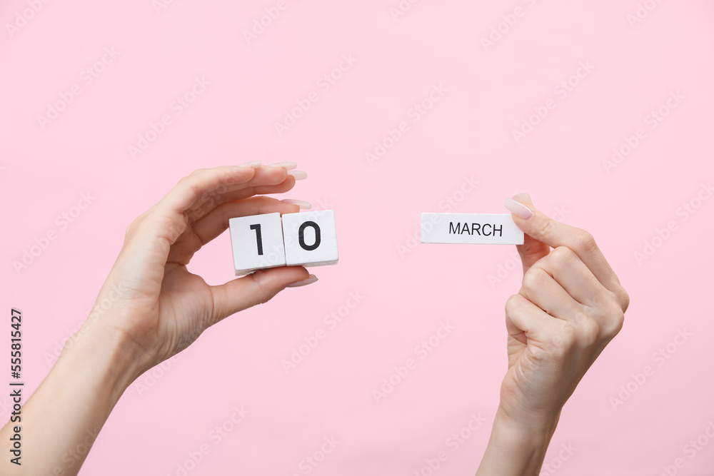 Woman's hands hold wooden block calendar with the date march 10 on pink background Woman's hands hold wooden block calendar with the date march 10 on pink background