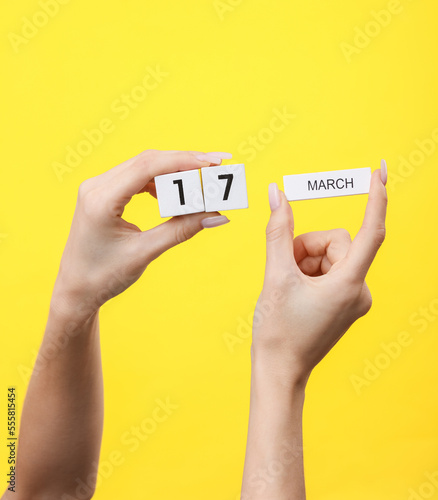 Woman's hands hold wooden block calendar with the date march 17 on yellow background