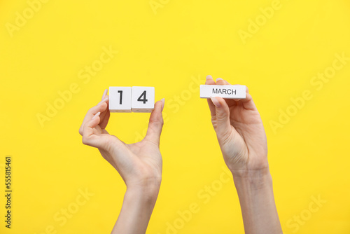 Woman's hands hold wooden block calendar with the date march 14 on yellow background