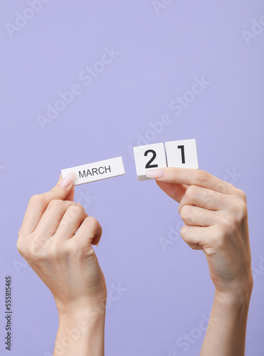 Woman's hands hold wooden block calendar with the date march 21 on pastel lavender color background