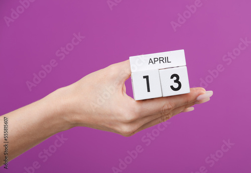 Block calendar with date april 13 in female hand on purple background