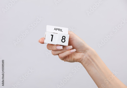 Block calendar with date april 18 in female hand on gray background