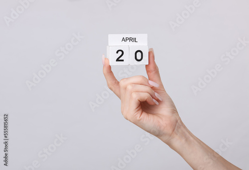 Block calendar with date april 20 in female hand on gray background