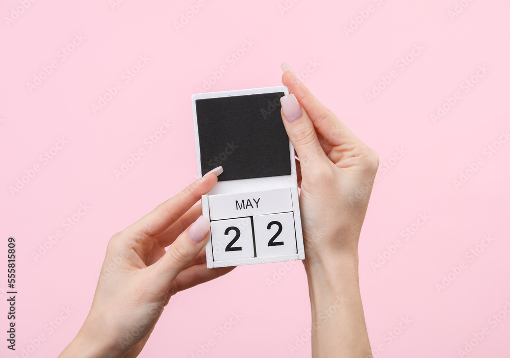 Block calendar with date may 22 in female hands on pink background Block calendar with date may 22 in female hands on pink background