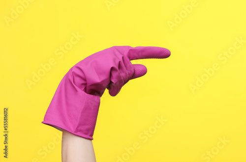 Hand in purple rubber cleaning glove points to the side on a yellow background. House cleaning and housekeeping concept