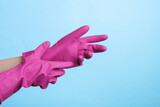 Hands wear purple rubber cleaning gloves on a purple background. House cleaning and housekeeping concept