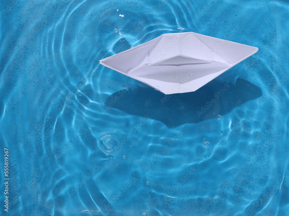 Fototapeta premium Paper boat floats in blue water with shadows. Top view