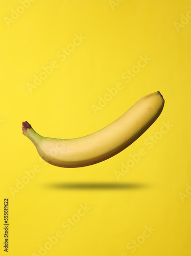 Ripe banana levitates on yellow background with shadow