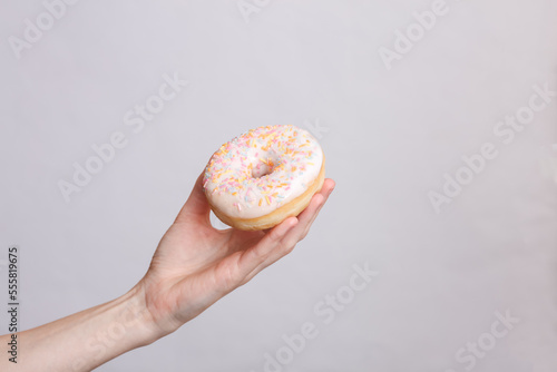 Glazed donut in a female hand on a gray background