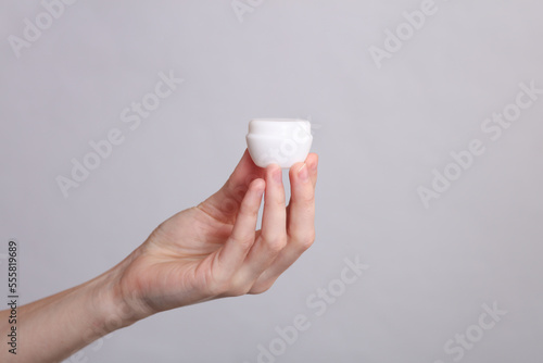 Woman's hand holds white jar of cream on a gray background