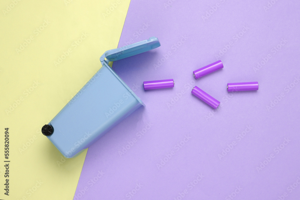 Battery recycling concept. Miniature trash can with aa batteries on colored background. Top view Battery recycling concept. Miniature trash can with aa batteries on colored background. Top view