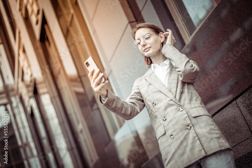 Wallpaper Mural Young modern business woman in a jacket and glasses looking at the screen of a smartphone in the city Torontodigital.ca